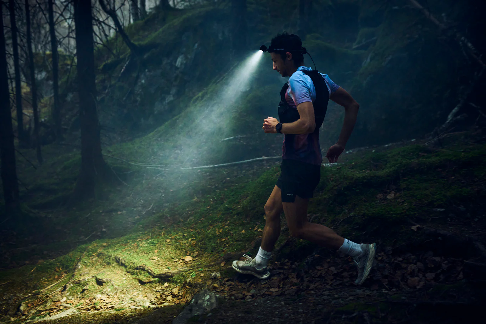 Coureur de trail avec frontale dans la forêt, descente technique de nuit