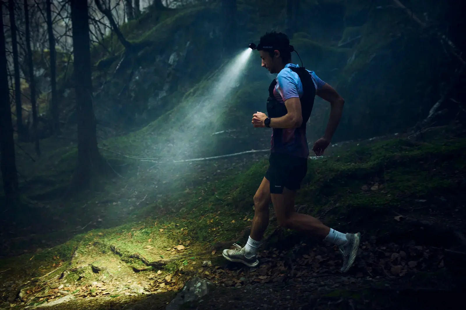 Coureur de trail avec frontale dans la forêt, descente technique de nuit